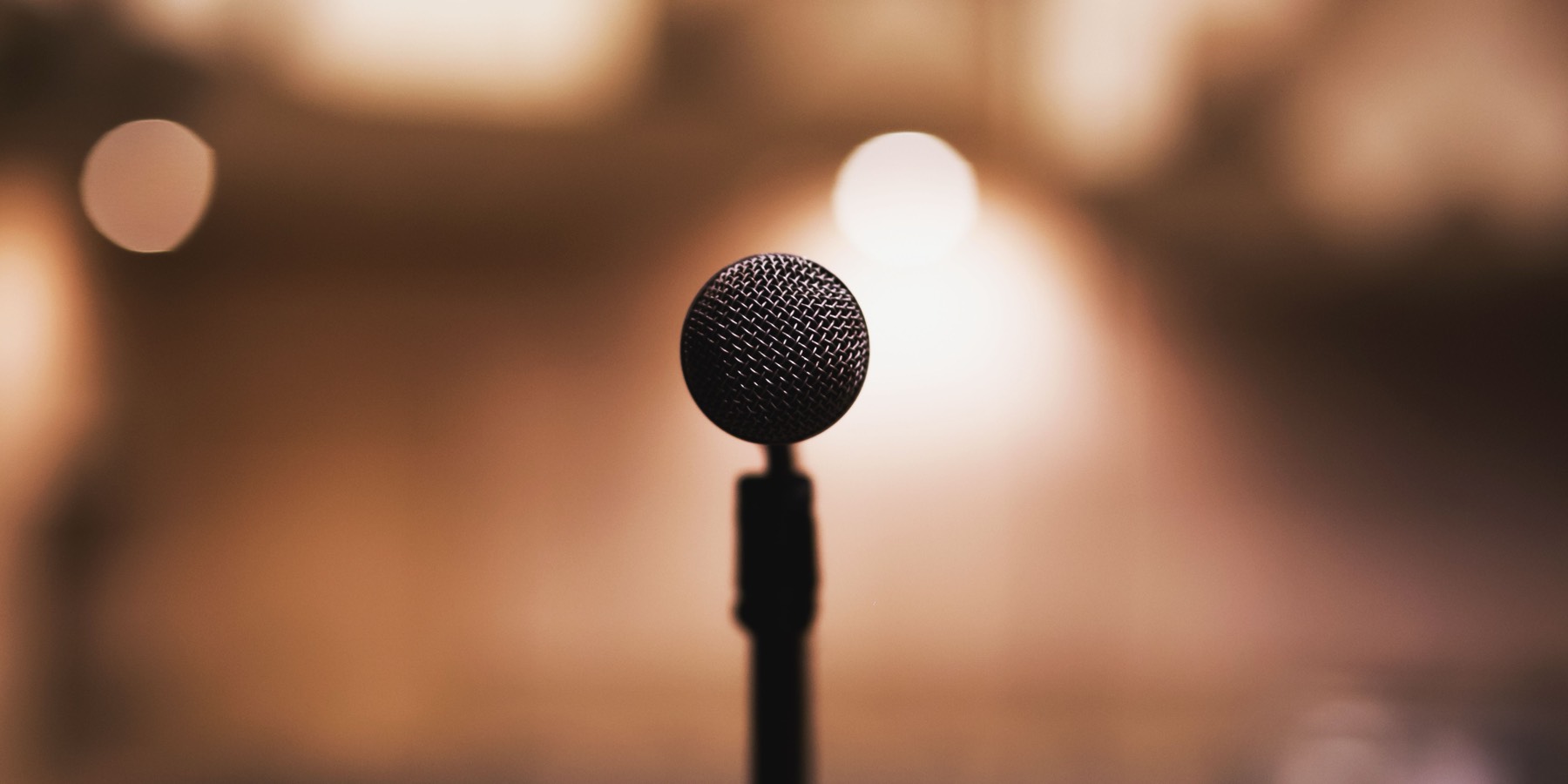 A microphone on a stand, lit against a darkened auditorium.