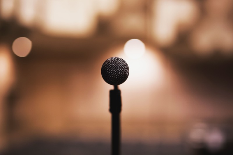 A microphone on a stand, lit against a darkened auditorium.